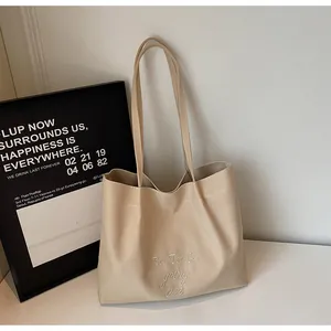 Détail de la broderie de lettres sur un sac cabas en toile beige avec de longues anses