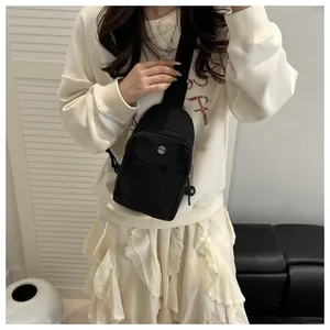 Detail of black nylon chest bag with silver M logo worn by model in a casual setting