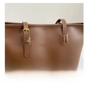Detail of golden metal buckle and letter print on brown leather tote bag shoulder strap
