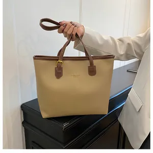 Detail of a large beige and brown tote bag showing the handles and gold metal hardware