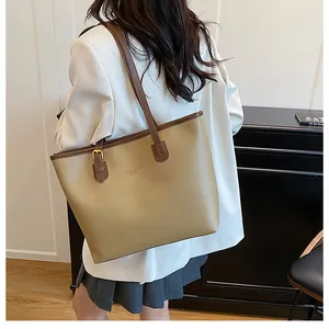 Back view of a khaki large tote bag with brown trim and logo detail on woman's shoulder