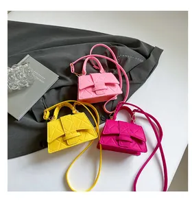 Three quilted mini crossbody bags in pink, yellow and rose on a stylish grey coat