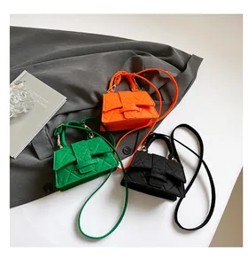 Close-up of three mini quilted handbags in orange, green, and black with long straps