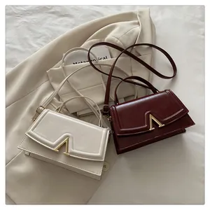 Close-up of sleek square handbag with V-shaped gold buckle on a beige blazer background