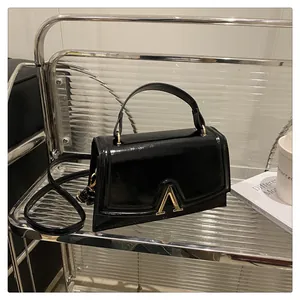 Close-up of black patent leather handbag featuring a prominent gold letter A metal buckle