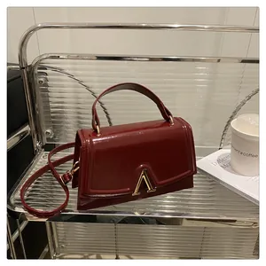 Detail of burgundy glossy leather bag with gold V-logo and flap closure detail