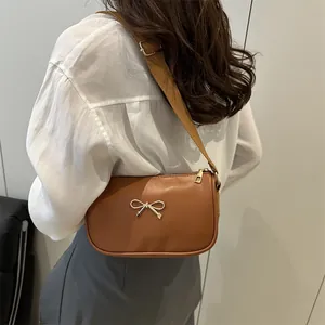 Sac bandoulière marron en cuir avec nœud doré et large sangle porté par un modèle