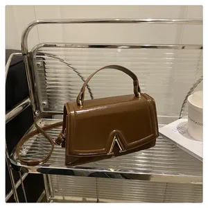 Detail view of brown glossy leather handbag with gold V-shape buckle on a metal stand