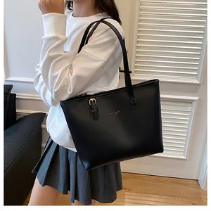 Detail of minimalist black leather tote bag with gold hardware and shoulder strap on model
