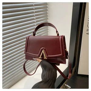 Detailed view of dark red glossy leather handbag with gold metallic V-shaped clasp