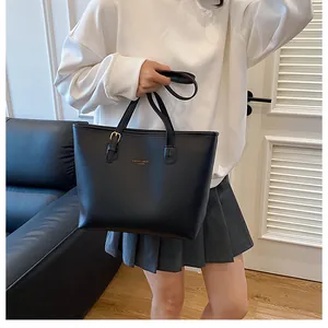 Black leather tote bag detail with gold brand logo and adjustable shoulder strap buckle
