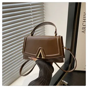 Detail view of deep brown trapezoid handbag with gold V-metal closure and textured finish