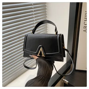 Macro detail of black leather crossbody bag with a gold V-shaped buckle and metal hardware