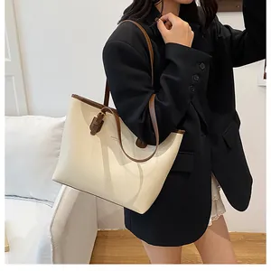 Close-up of beige leather tote bag with brown straps worn by a model in a minimalist setting