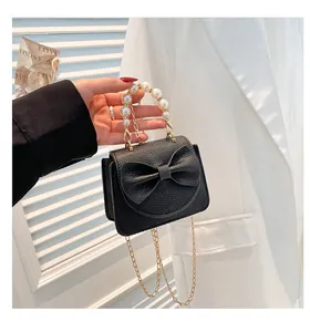 Detail of black pebbled leather mini bag with pearl handle and bow decoration