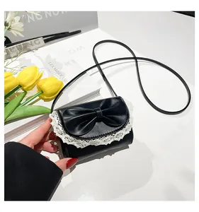 Detail of small black flap bag featuring a large leather bow and white lace trim edge