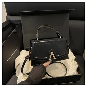 Glossy black leather crossbody bag with V-shaped gold buckle in elegant gift box setup