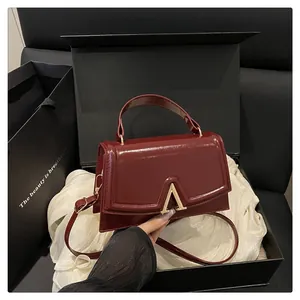 Detail of burgundy glossy handbag with gold V-buckle on elegant gift packaging