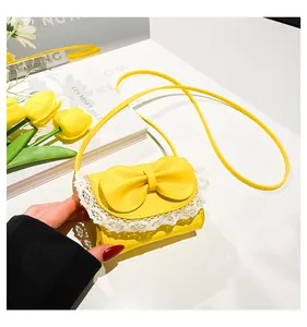 Detail of yellow mini shoulder bag with large bow and white lace trim on the flap