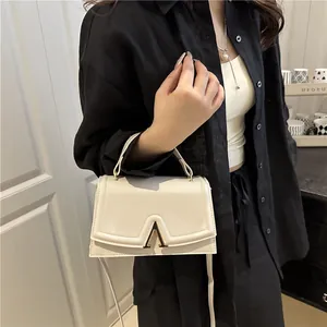 Chic beige leather top handle bag with gold V clasp shown on model with shoulder strap