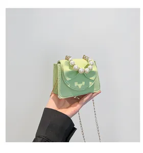 Detail of light green mini bag with bow design, pearl handle and gold chain strap