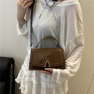 Brown glossy leather trapezoid handbag with gold V buckle on a female model