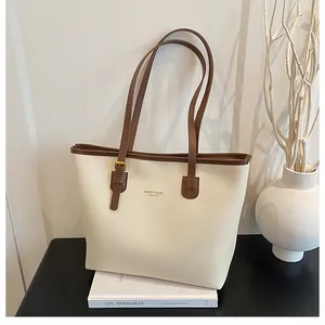 Close-up of minimalist cream tote bag with contrast brown handles and gold logo detail