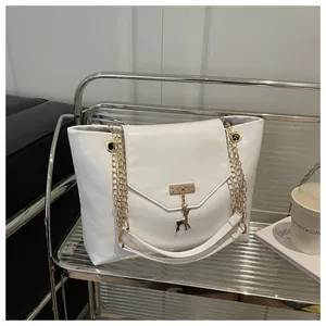 Detail of white PU leather tote with golden deer charm and chain strap on metal shelf