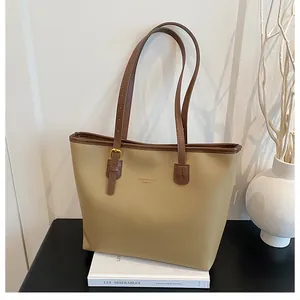 Detail of khaki tote bag with brown trim, logo print, and gold buckle on books