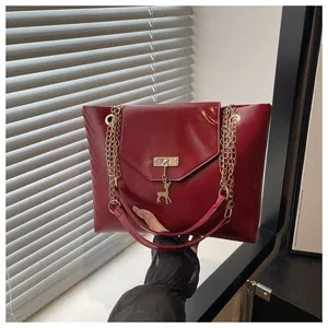 Detail of burgundy high-gloss leather bag with gold deer charm and chain strap