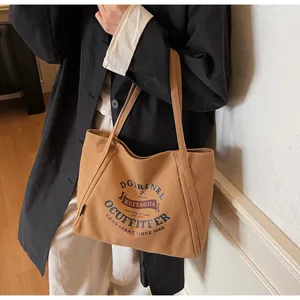 Bolso tote de lona caqui con letras azules mostrado llevado al hombro de forma elegante
