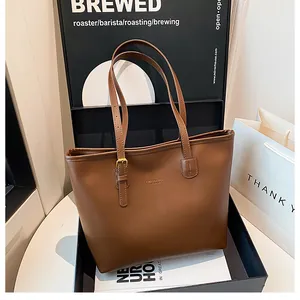 Detailed view of brown leather tote bag with gold logo lettering and metallic buckle strap