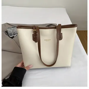 Chic cream and dark brown tote bag on a bed with a grey blazer and accessories