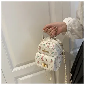 Detail of white mini backpack with cartoon prints, gold chain, and FASHION metal logo