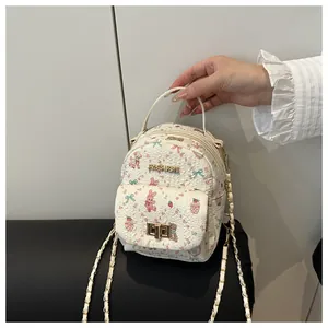 Detail of a creamy white mini backpack with pink cartoon patterns and a gold lock