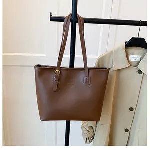 Brown matte PU leather tote bag with long straps and gold buckle hanging on a rack