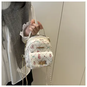 Detail of white mini floral backpack featuring golden metal logo and chain strap texture
