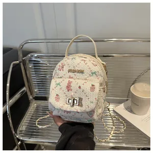 Detail of cream mini backpack with cartoon patterns, gold chain, and metal turn-lock buckle
