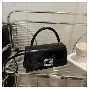 Detail of glossy black patent leather handbag with sparkling rhinestone G-buckle closure