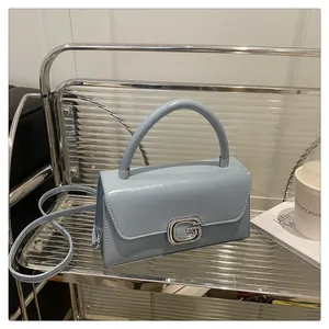 Close-up of light blue patent leather handbag with sparkling rhinestone G-buckle detail