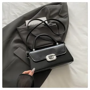 Detail of glossy black leather handbag with rhinestone G-buckle on a gray blazer