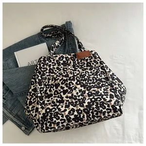 Détail du sac cabas imprimé léopard avec bordure en cuir marron et rivets métalliques à l'avant
