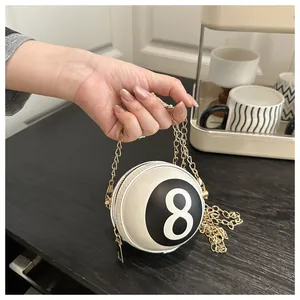 Detail of a mini round billiard No. 8 crossbody bag with gold chain strap in hand