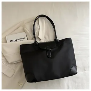 Detail of black nylon tote bag with leather accents on a beige blazer background