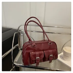 Détail d'un sac d'épaule en cuir verni bordeaux avec double poches et boucles argent