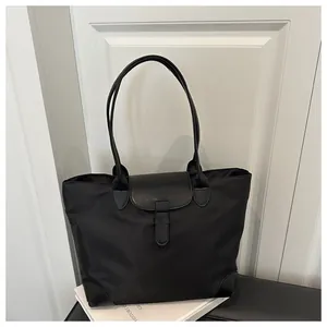 Detail of black nylon tote bag featuring a leather flap closure and slim shoulder strap