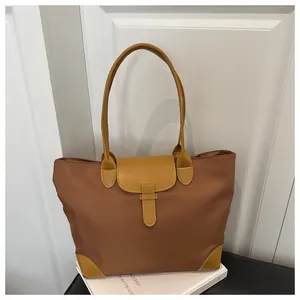 Detail of a brown nylon tote bag with mustard yellow leather trim and flap closure