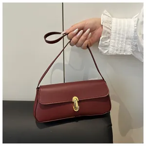 Close-up of burgundy leather underarm bag featuring a metallic golden capsule lock