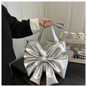 Dettaglio della borsa tote argento con fiocco metallico, tenuta a mano dal vivo