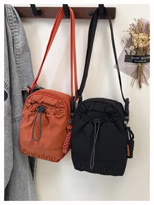 Detail of drawstring crossbody phone bags in black and orange with textured nylon and embroidery